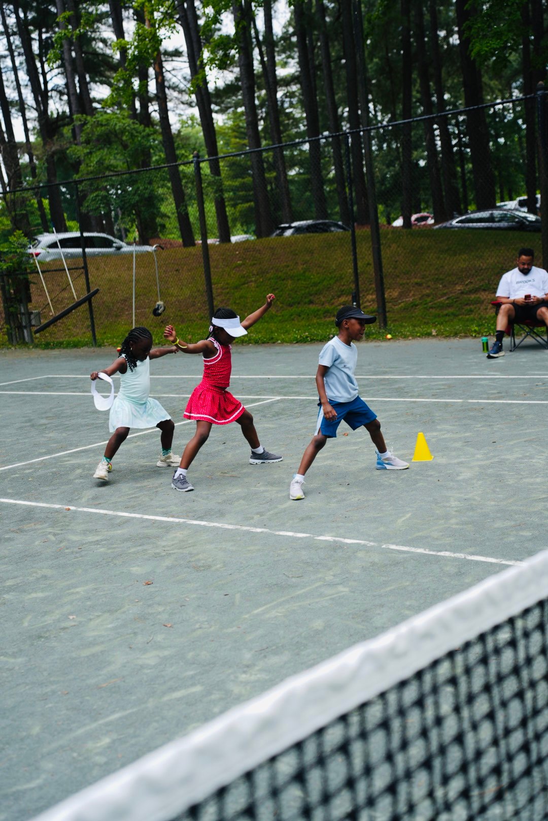 Three kids running a tennis drill at a Miles Ahead Foundation clinic